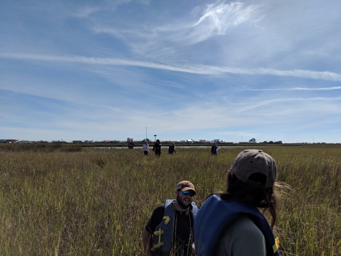 Students walking through a marsh with clouds overhead.