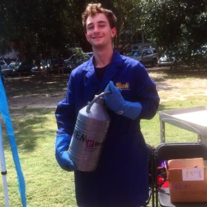 Undergraduate worker Andrew in a lab coat holding a metal tank