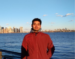 Photo of Ashwani Rai smiling in front of a body of water with a city skyline in the background