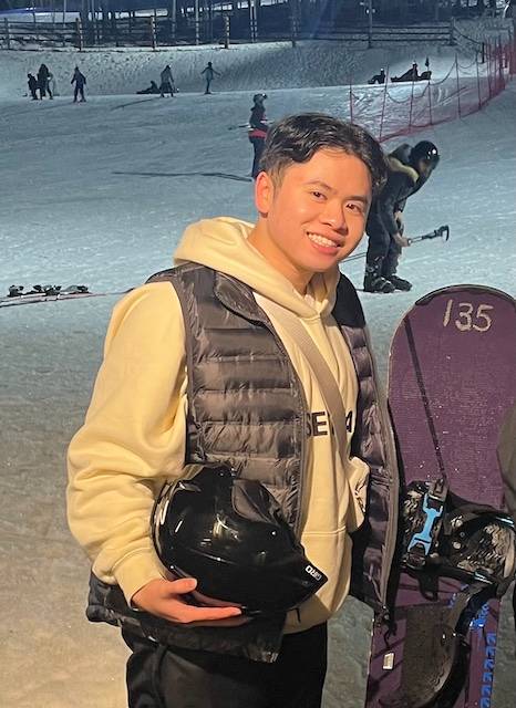 Photo of Jacob smiling in snow next to a snowboard