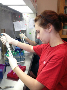 Photo of Jennifer Quebedeaux working in the laminar flow hood, holding a pippette