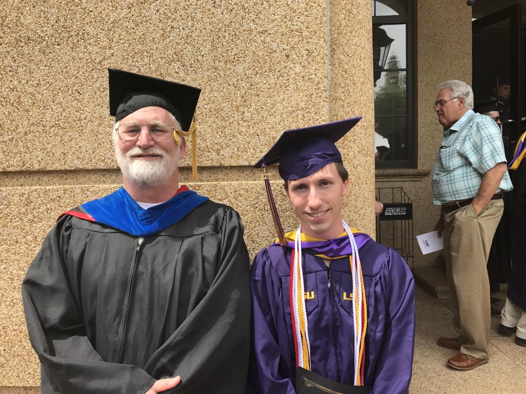 Dr. Moroney and Josh both in graduation regalia standing side-by-side smiling
