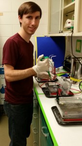 Photo of Josh Schwartzenburg in the lab holding a pippette over a gel electrophoresis tank