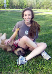 Photo of Julie Cronan smiling in a patch of grass with a dog