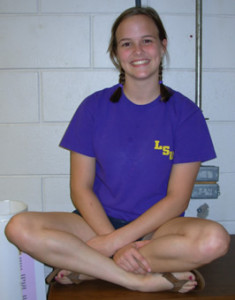 Photo of Rachel Yates smiling, sitting on a surface with legs crossed