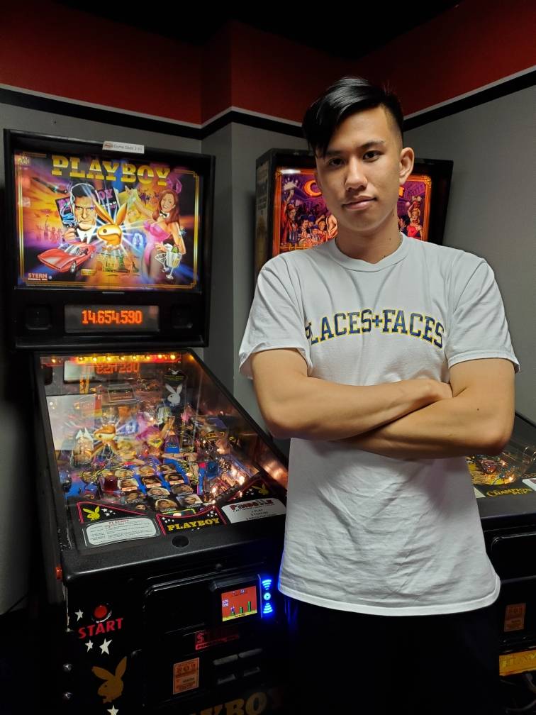 Photo of undergraduate Timothy Chen standing with arms crossed in front of a pinball machine
