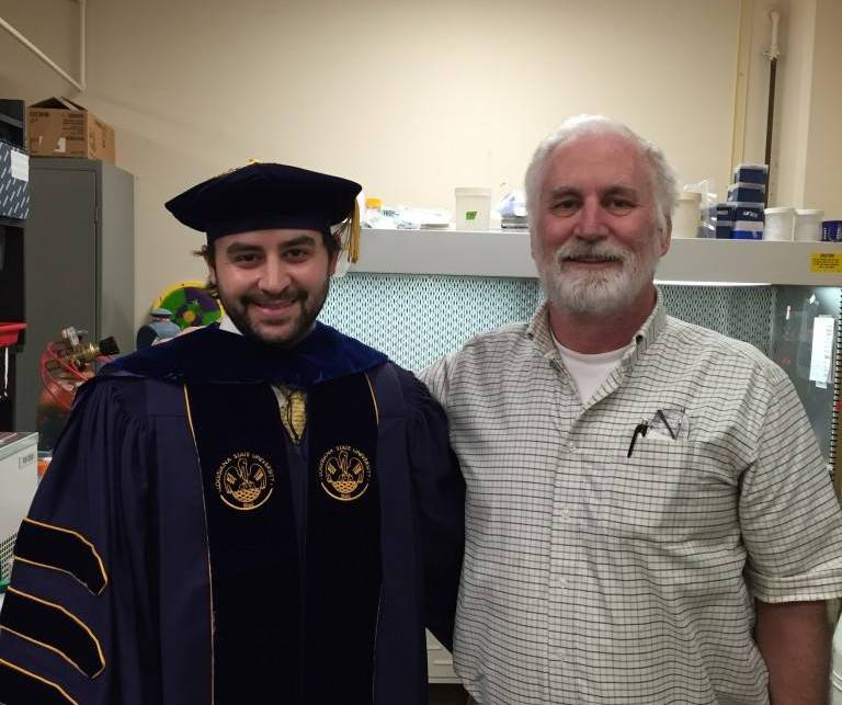 Photo of Wes Frey in graduation regalia smiling side-by-side with Dr. Moroney