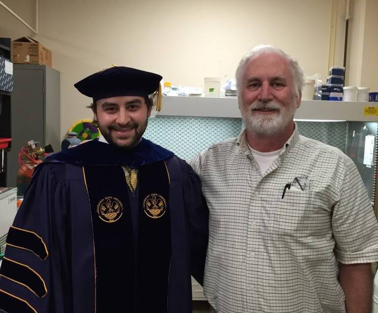 Dr. Moroney and Wes standing side-by-side smiling, Wes is in his graduation regalia