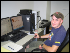 Andrew F. sitting at computer wearing cap