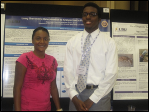 Stephanie D. & Blaise C. smiling in front of poster
