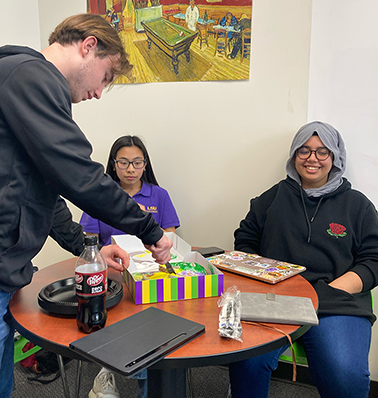 Student are celebration for Mardi-Gras. Briggs is cuttine Mardi-Gras cake.