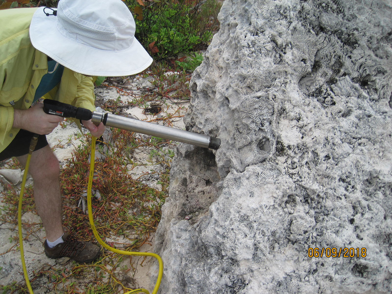 A man using a coring rod to core a coral boulder 