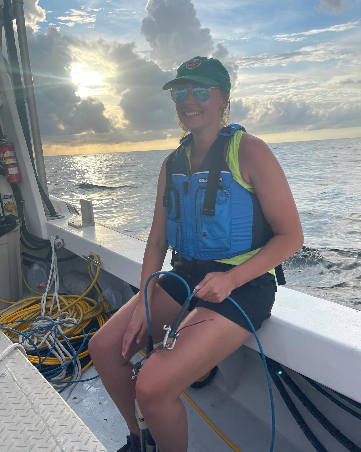 Masters student, Kendall Brome smiling while sitting on a boat for field work. She is holding a censor for the sound velocity profiler.