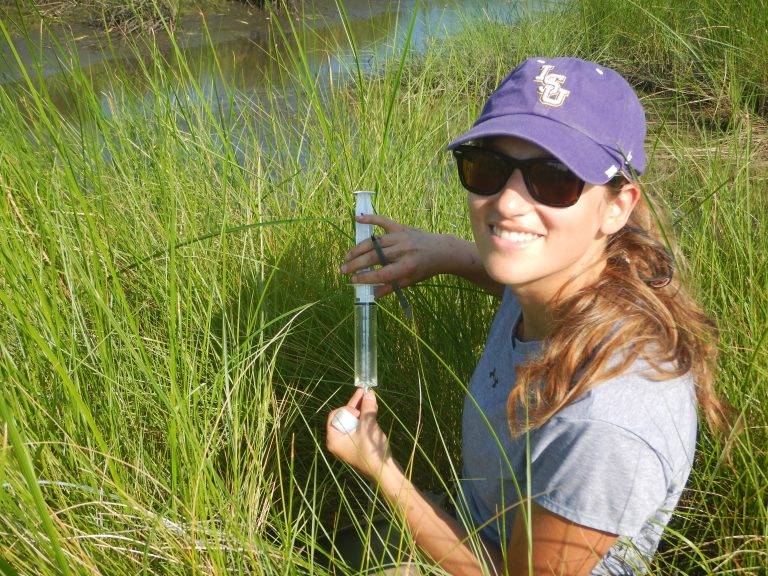 Woman in a wetland surrounded by grasses and holding a syringe.