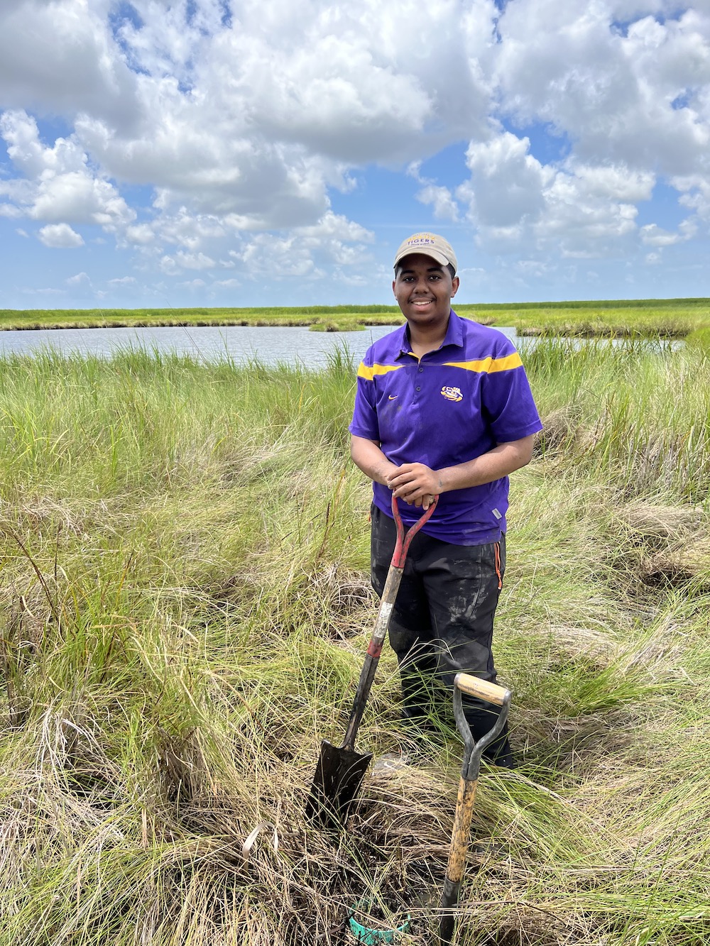 Man standing in a marsh holding a shovel.