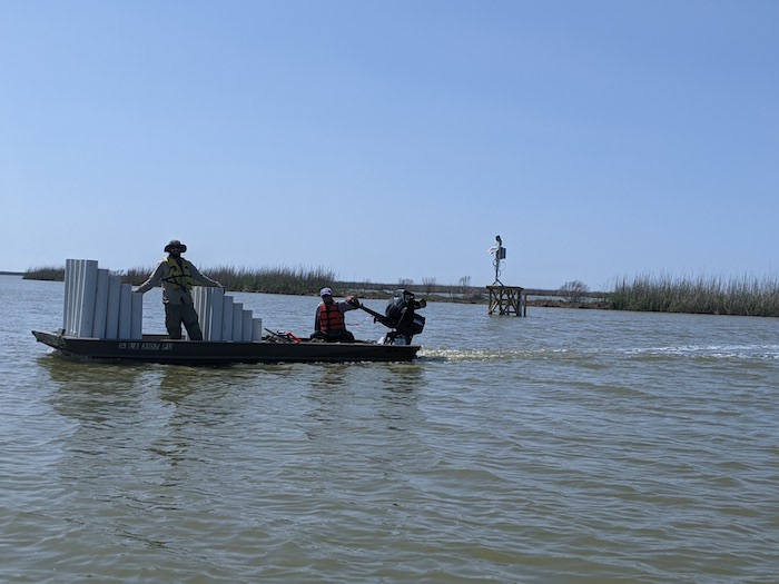 People riding in a shallow boat with lots of pvc pipes (Marsh Organs)