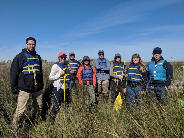 Students wearing life jackets while standing in a marsh.