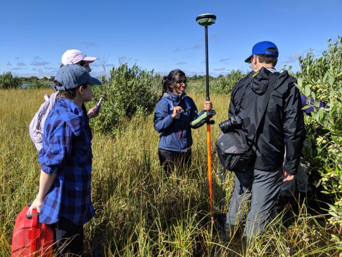 Students working in a marsh, with one student holding a GPS device attached to a pole.