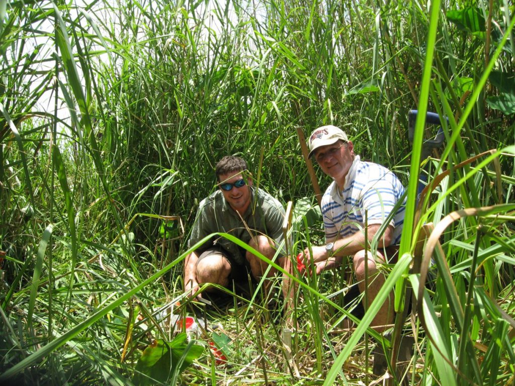 two men crouch in tall grass