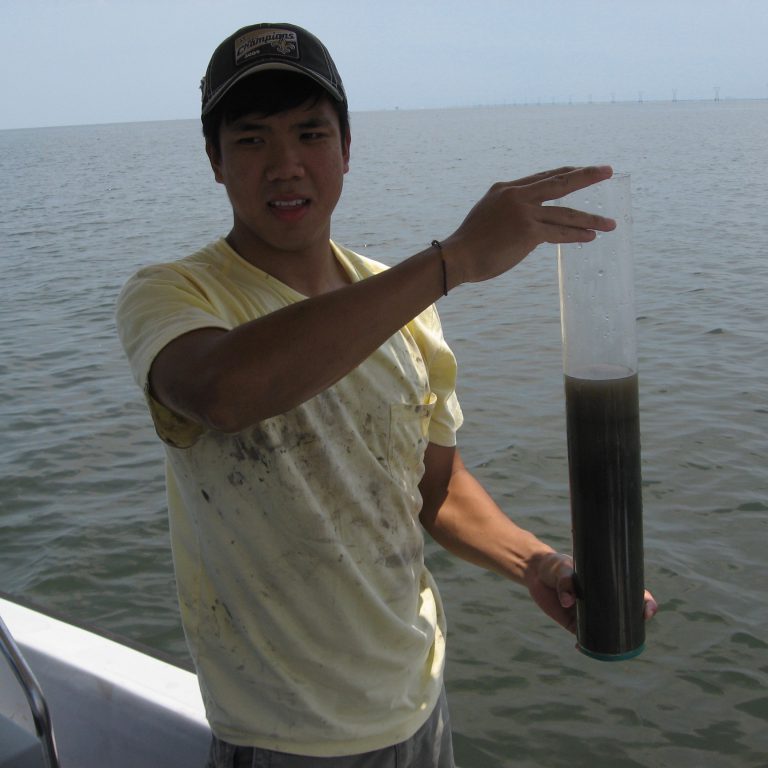 a man holds up a soil core; water is visible behind him